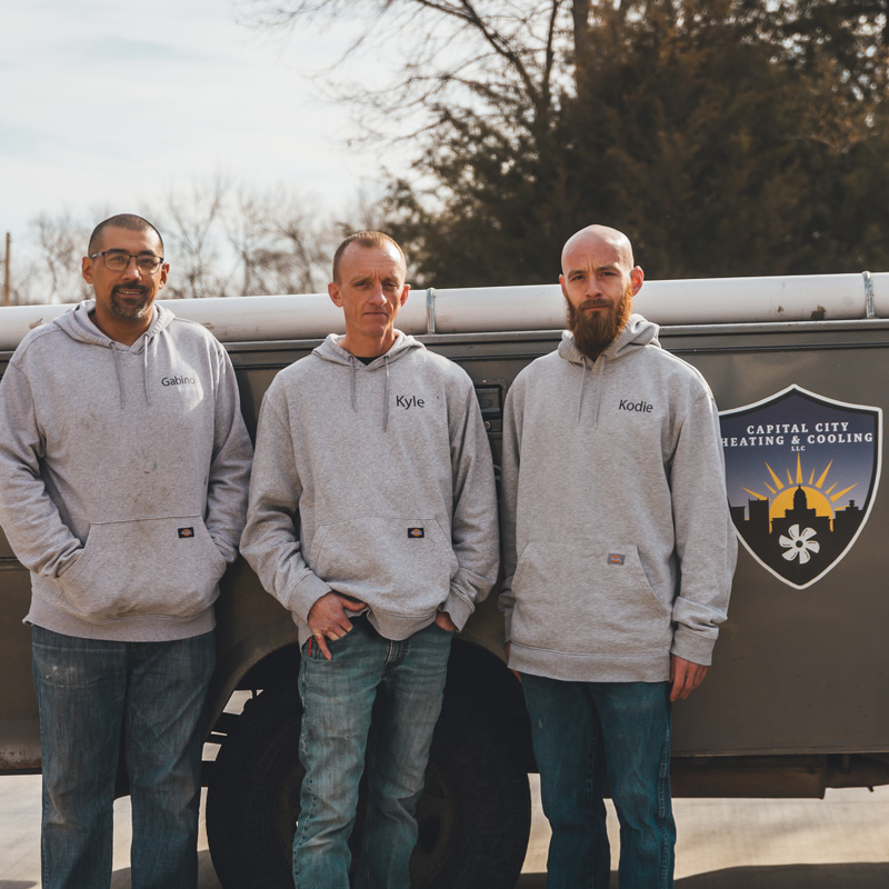 three guys standing in front of capital city heating and cooling sign on a truck